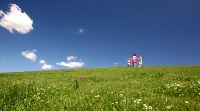 stock-footage-woman-with-children-holding-hands-descend-hill-with-green-grass